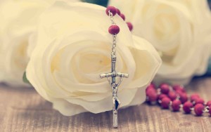 Catholic rosary and white roses on wooden background. Religion concept.